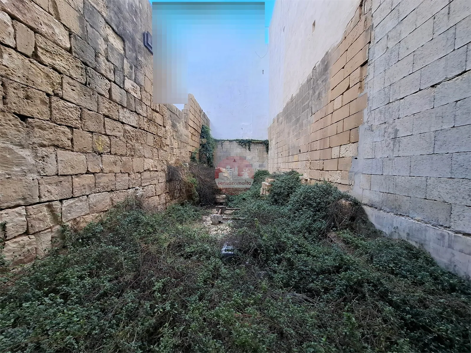 Long enclosed backyard with exposed stone boundary walls in shell condition